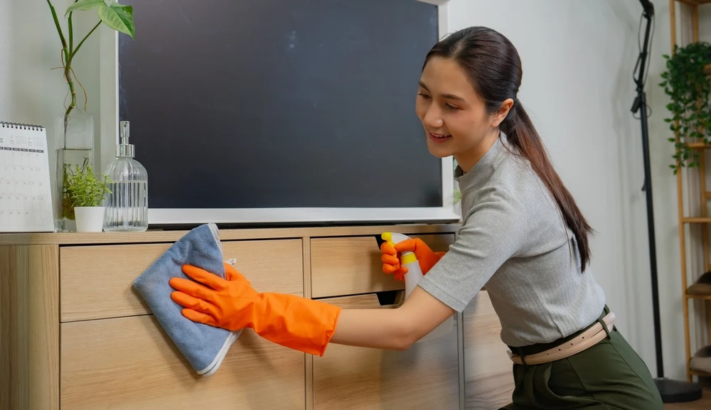 A woman in orange gloves cleaning a wooden cabinet in a home
