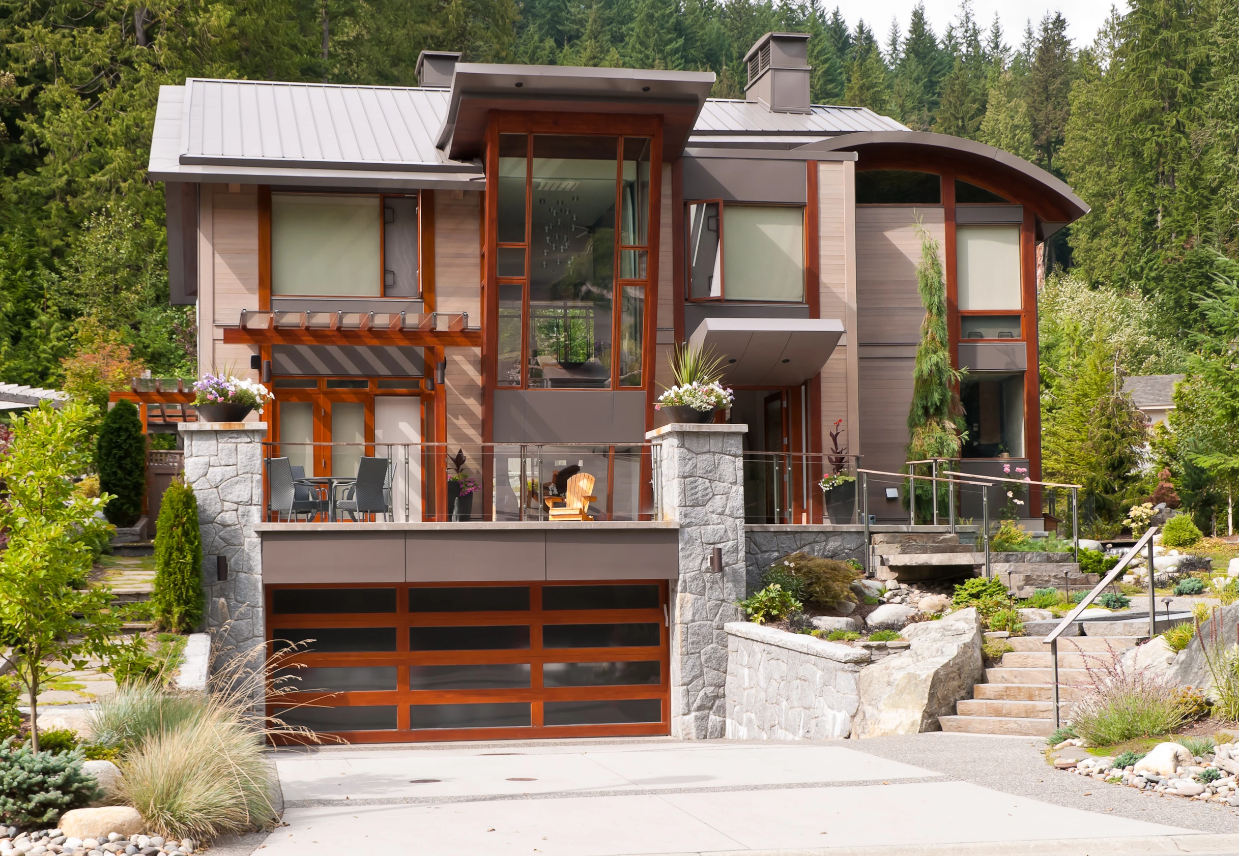 Modern luxury Montana home featuring stone retaining walls, beautiful landscaping, and a wooden glass garage door