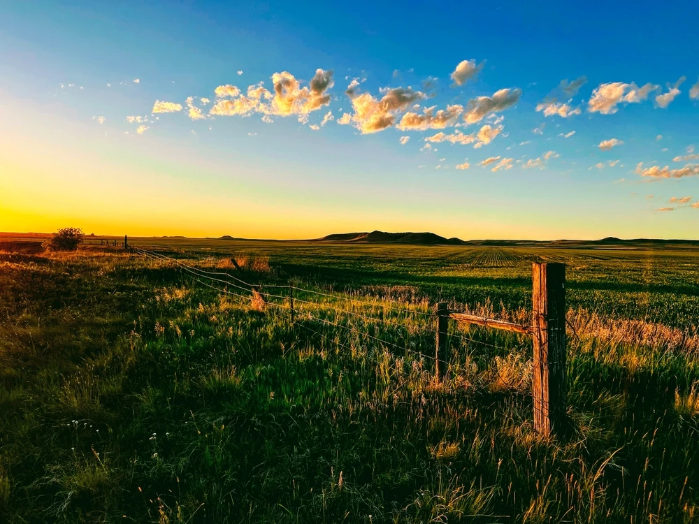 A wooden fence running through an open Montana valley at sunset